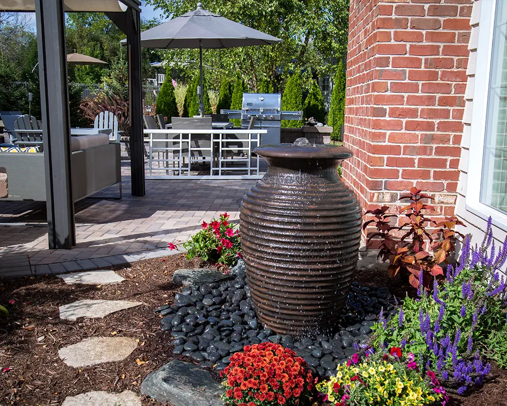 Decorative urn fountain near a brick wall with surrounding flowers, enhancing backyard patio ambiance.