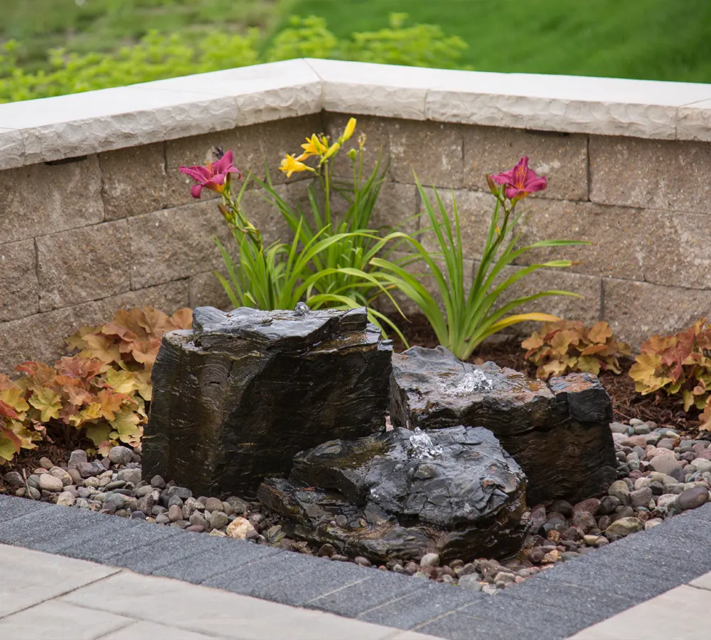 Rock fountain with decorative flowers in a landscaped garden, showcasing a durable and natural water feature.