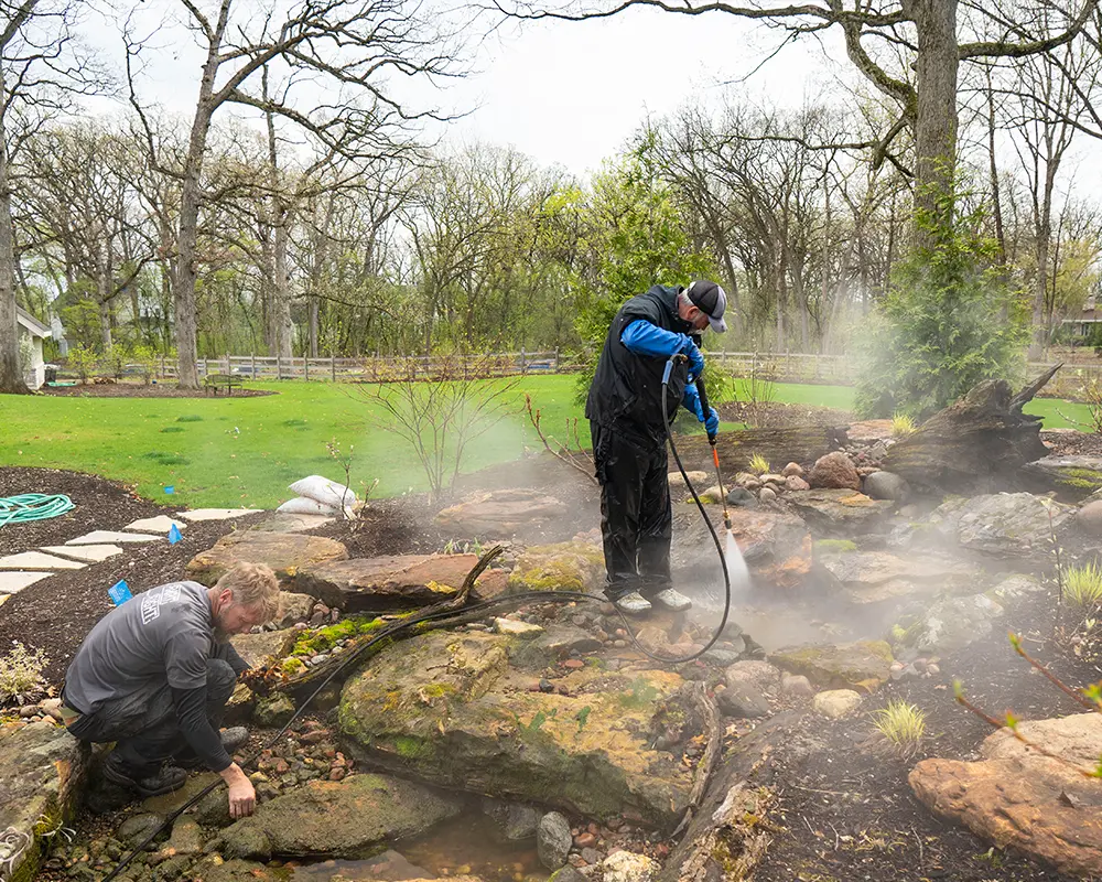 Professional pond cleaning with pressure washer to remove algae and restore water quality in a residential garden