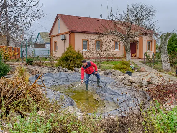 Technician performing pond maintenance in a residential garden, cleaning and removing debris from the pond liner