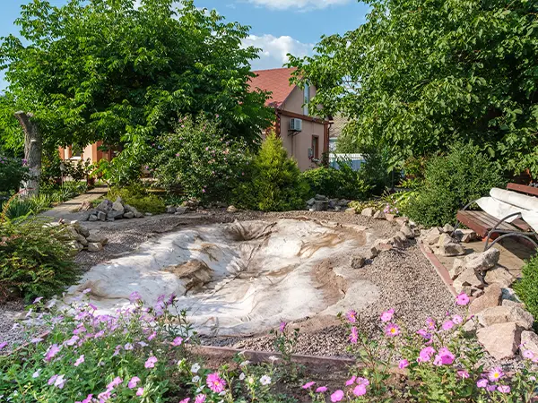 Backyard pond under repair with exposed liner and surrounding plants in a landscaped garden