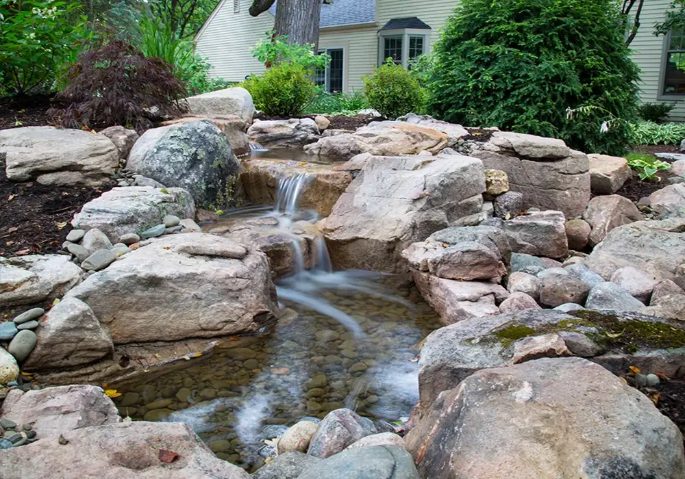 Close-up of pondless waterfall with flowing water over stacked stones in a landscaped garden