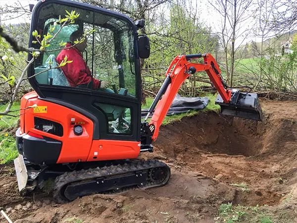 Excavator preparing backyard ground for water feature installation, handled by an expert building team.